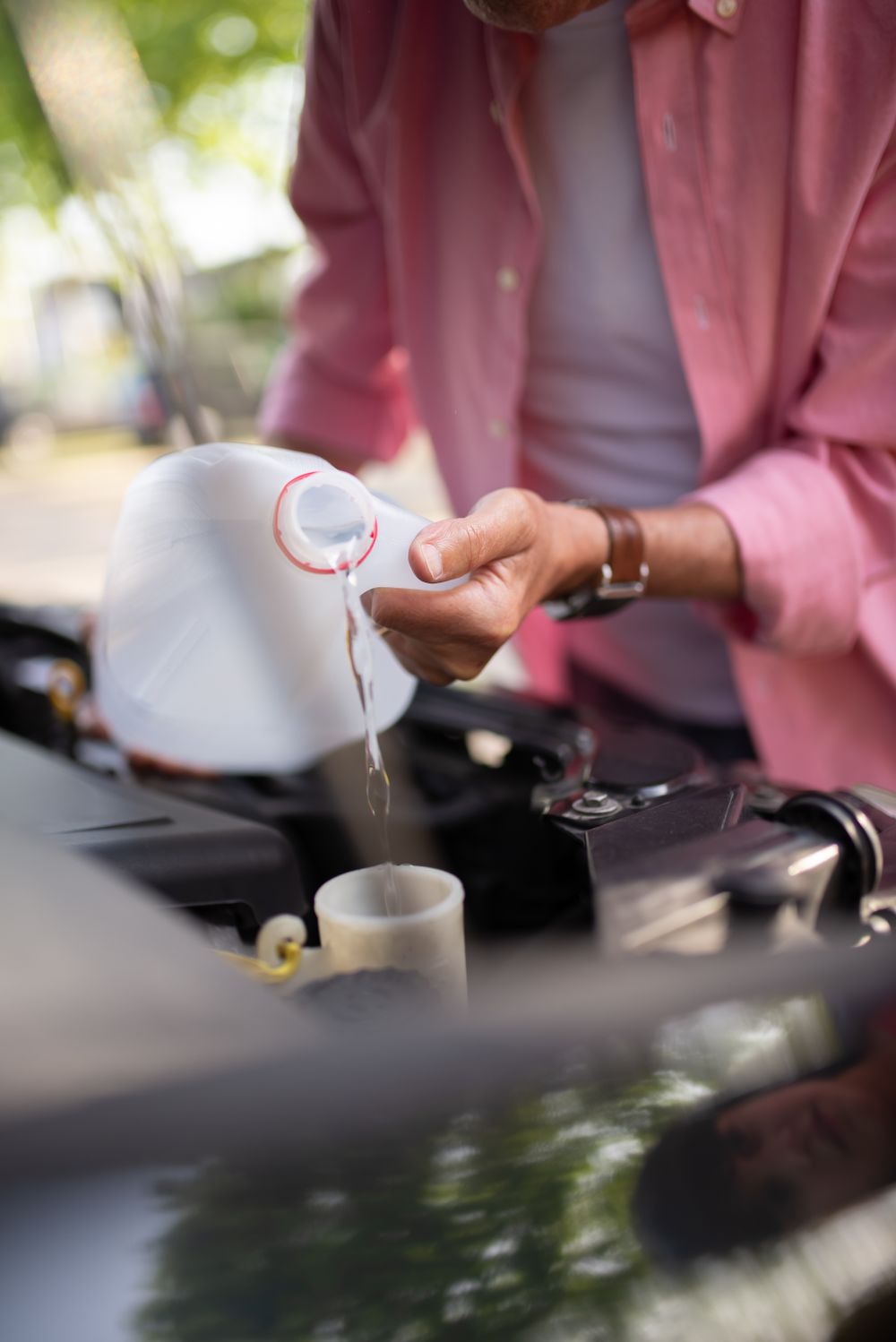 Hands refilling the windshield-washer reservoir under an open hood