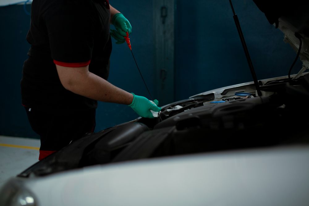 Gloved technician examining an oil dipstick beside an open engine bay